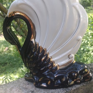 May include: A white ceramic swan figurine with black and gold accents. The swan has a wide wingspan and a detailed design.