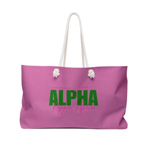 May include: A pink tote bag with white rope handles and a green and pink "ALPHA Kappa Alpha 1908" logo.