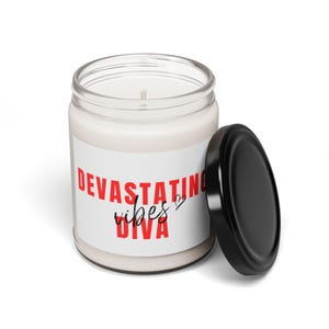 May include: A white candle in a glass jar with a black lid. The jar has a white label with the text "DEVASTATING vibes DIVA" in red and black.