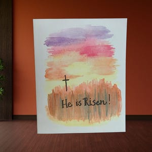 Juego de tarjetas de felicitación minimalistas con forma de cruz de Pascua, diseño de acuarela de un atardecer escénico, juego de tarjetas religiosas festivas hechas a mano, con la frase "¡Ha resucitado!" preescrita.