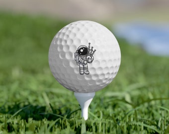 Pode incluir: Uma bola de golfe branca com uma ilustração em preto e branco de um astronauta tocando gaita de foles.