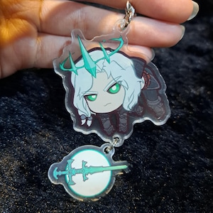 May include: A clear acrylic keychain featuring a cartoon character with white hair, a green crown, and a green sword. The character is wearing a black and white outfit and is holding a sword.