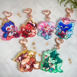 May include: Set of seven colorful character keychains featuring a variety of characters with different expressions and poses. The keychains are made of clear acrylic with a gold metal ring.