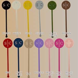 Op de afbeelding: Een verzameling van twaalf drankroerstaafjes in verschillende kleuren, waaronder zwart, wit, goud, zilver, olijfgroen, bruin, rood, marineblauw, tan, paars, pastelroze, felroze en ros&eacute;goud. Elke roerstaaf heeft de letters "SC".
