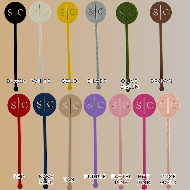 Op de afbeelding: Een verzameling van twaalf drankroerstaafjes in verschillende kleuren, waaronder zwart, wit, goud, zilver, olijfgroen, bruin, rood, marineblauw, tan, paars, pastelroze, felroze en ros&eacute;goud. Elke roerstaaf heeft de letters "SC".