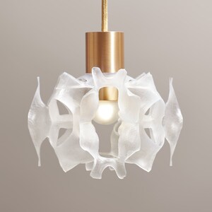 May include: A white, translucent pendant light fixture with a gold metal canopy and a single light bulb. The fixture is made of a delicate, organic-looking material that resembles a flower.