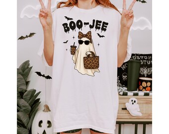 May include: White t-shirt with a graphic of a ghost wearing sunglasses, a bow, and carrying a purse and coffee. The text "BOO-JEE" is above the ghost. The shirt has a relaxed fit and is suitable for Halloween.