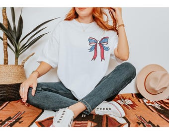 May include: A white t-shirt featuring a red, white and blue bow with stars.
