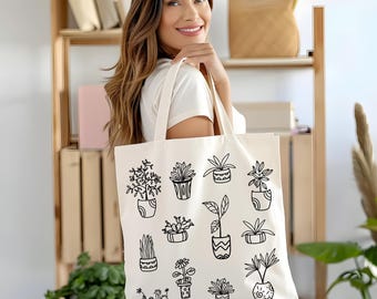 May include: Cream-colored tote bag featuring black line drawings of various potted plants. The bag is held by a person wearing a white t-shirt. The background includes wooden shelves and greenery.