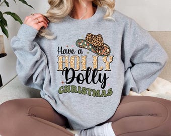 May include: A gray sweatshirt with the text "Have a Holly Dolly Christmas" in a mix of fonts and colors. The design includes a cowboy hat with a leopard print crown and floral accents, perfect for the holiday season.