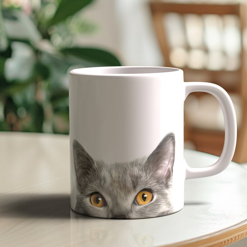 May include: A white ceramic mug with a gray cat peeking over the rim. The cat has yellow eyes and a gray nose.