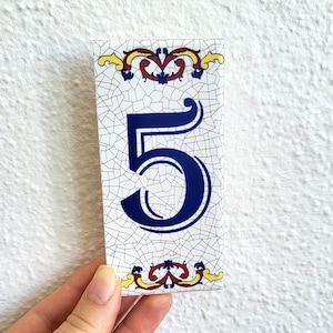 May include: White ceramic tile with a blue number "5" in a decorative font. The tile has a crackled glaze and is decorated with yellow and red floral designs.