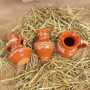 May include: Three small terracotta pottery vases with white painted designs. The vases are sitting on a bed of straw.