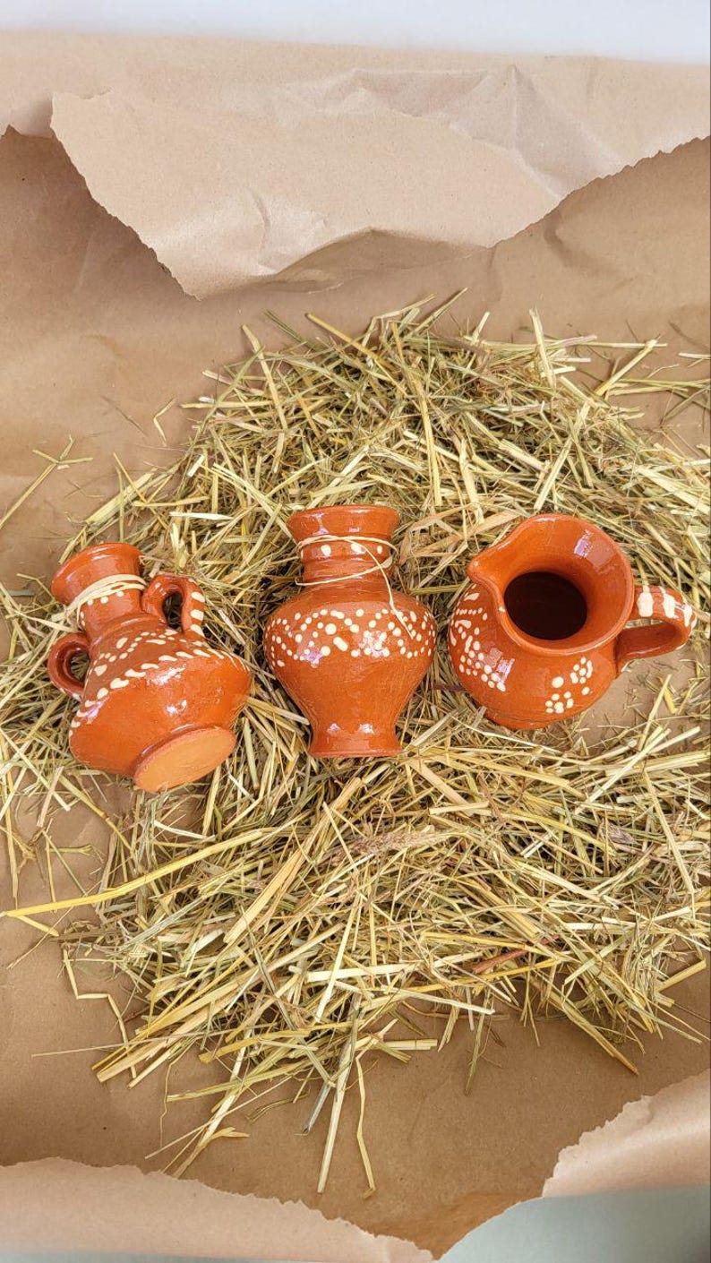 May include: Three small terracotta pottery vases with white painted designs. The vases are sitting on a bed of straw.