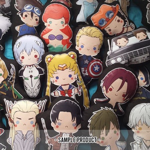 Pode incluir: Uma cole&ccedil;&atilde;o de pequenas almofadas de pel&uacute;cia com v&aacute;rios personagens de anime e cultura pop, incluindo uma sereia, um super-her&oacute;i com escudo, uma guerreira sailor e um carro preto com o texto SAMPLE PRODUCT impresso na parte inferior.