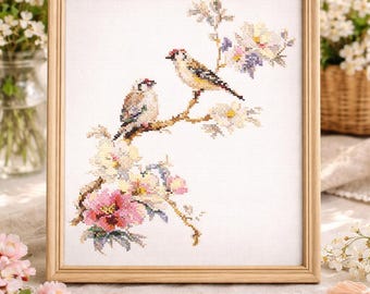 May include: Cross-stitch artwork in a wooden frame. The embroidery depicts two birds perched on a flowering branch with pink, white, and purple blossoms. The background is a soft white fabric.