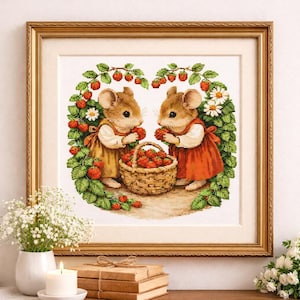 May include: Framed cross-stitch artwork depicting two mice in dresses, eating strawberries. A woven basket is filled with strawberries. The artwork is surrounded by a gold frame and a strawberry vine.