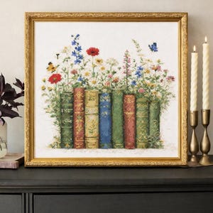 Puede incluir: Obra de arte de punto de cruz en un marco dorado que representa una fila de libros con lomos coloridos, adornada con una vibrante variedad de flores silvestres, mariposas y abejas. La obra de arte se exhibe sobre una cómoda negra, con velas en candelabros de latón.