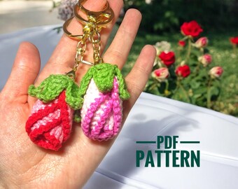Peut inclure: Deux porte-clés faits à la main en crochet en forme de fleurs, l'un rouge et blanc, l'autre rose et blanc, avec des feuilles vertes. Les porte-clés ont des anneaux dorés. Le texte "PDF PATTERN" est visible dans l'image.