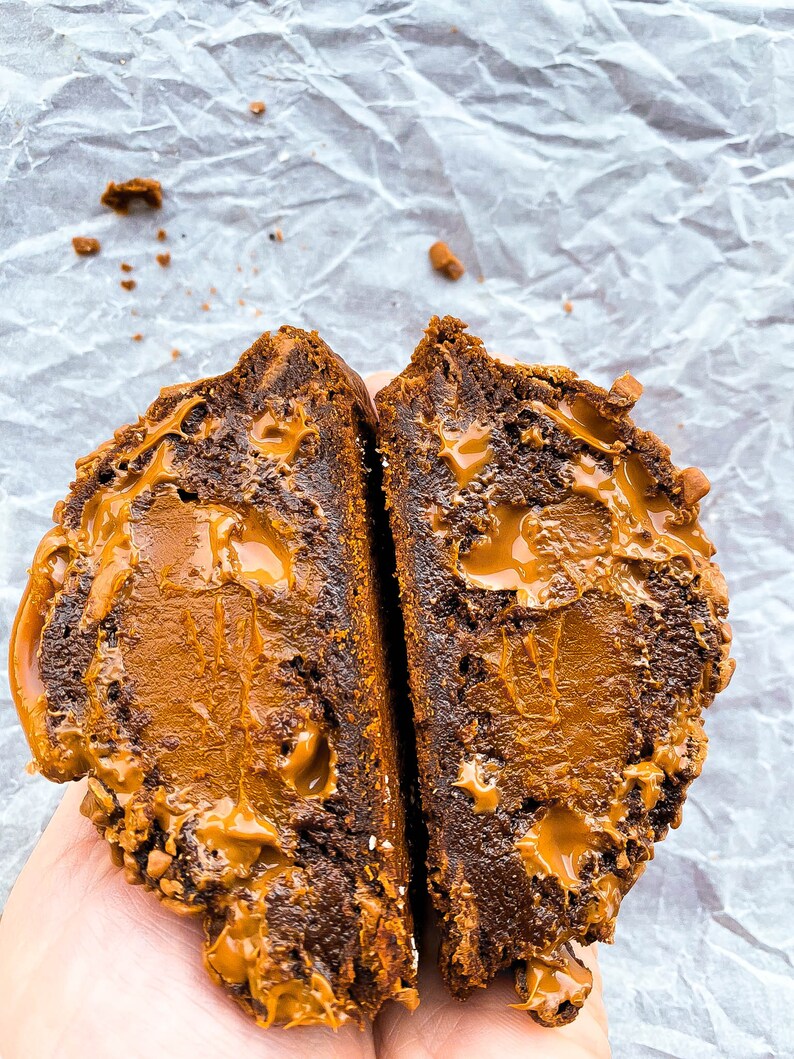 May include: Close-up of a chocolate cookie broken in half, revealing a gooey caramel filling.