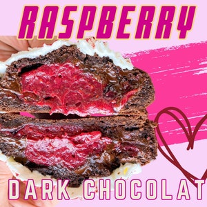 May include: A close-up of a chocolate cookie filled with raspberry jam. The cookie is split in half, revealing the red jam filling. The cookie is topped with white frosting and the words "RASPBERRY" and "DARK CHOCOLATE" are written in yellow on a pink background.