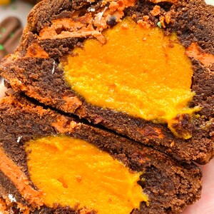 Pode incluir: Close-up de uma sobremesa de chocolate cortada ao meio com um recheio laranja brilhante. A sobremesa tem camadas de bolo marrom escuro e cobertura laranja. Uma pe&ccedil;a de chocolate branco com um centro marrom claro fica em cima.