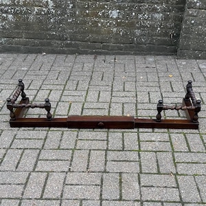 May include: A dark brown wooden fireplace fender with a rectangular base and two vertical side supports. Each side support features a decorative twisted spindle design with small spherical finials at the top and bottom of the posts.