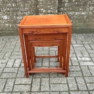 May include: A set of four wooden nesting tables in a reddish-brown finish. Each table is square with decorative carved details. The tables are designed to fit inside each other, offering a space-saving storage solution.