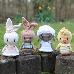 May include: Four crocheted stuffed animals: a white bunny, a brown bunny, a white lamb, and a yellow chick. The animals are sitting on a stone wall.