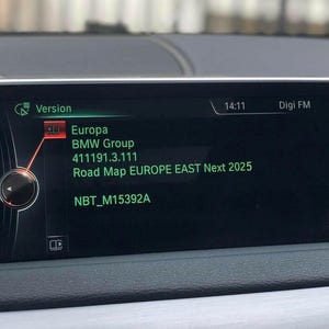 Puede incluir: La pantalla de infoentretenimiento de un coche muestra información del sistema. La pantalla muestra "Version", "Europa", "BMW Group" y "Road Map EUROPE EAST Next 2025". La hora es 14:11 y la radio está en Digi FM. La pantalla es negra con texto blanco y verde.