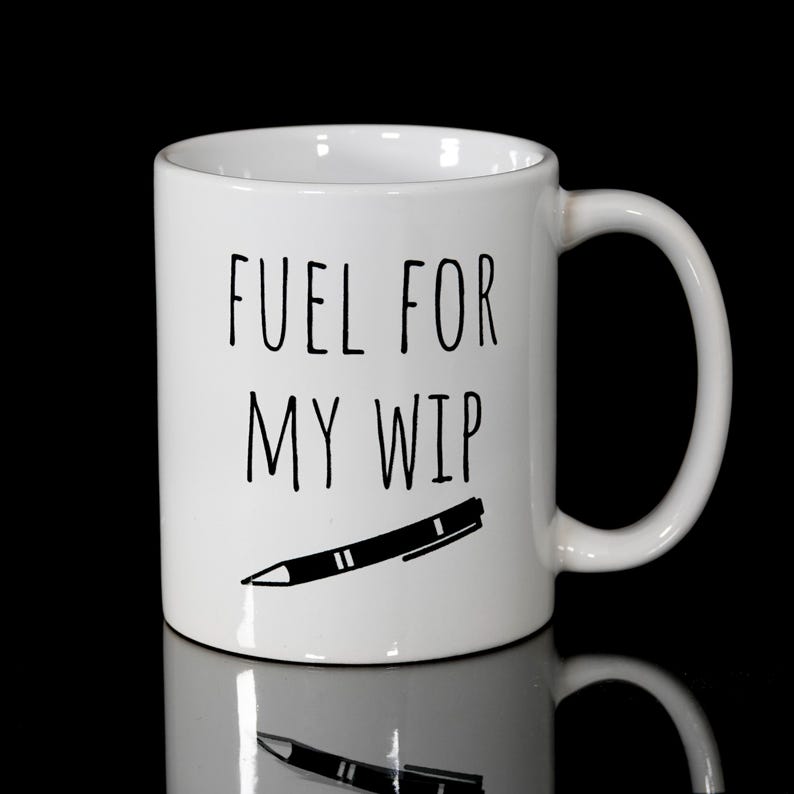 May include: White ceramic mug with the text "FUEL FOR MY WIP" in black, along with a black pen illustration. The mug has a curved handle and is set against a black background.