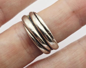 May include: A silver-toned ring with a textured, layered design. The ring features multiple bands that create a ribbed effect. The jewelry is worn on a finger, showcasing its metallic sheen and intricate details. This ring is a piece of fashion jewelry.