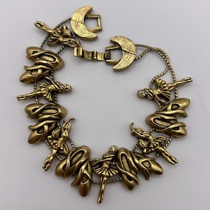 May include: Gold-toned bracelet featuring ballet-themed charms. The bracelet includes charms of ballet slippers and ballerinas in various poses. The clasp is a crescent moon shape. The bracelet is made of metal.
