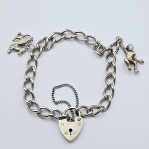 May include: Silver charm bracelet featuring a heart-shaped padlock clasp and chain links. The bracelet includes charms of a pegasus and a monkey. The bracelet is a vintage piece.