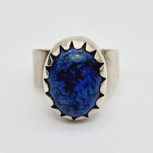Puede incluir: Un anillo de plata con una piedra de lapislázuli azul engastada en un diseño de estrella.