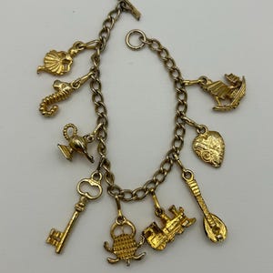 May include: Gold-coloured charm bracelet with a variety of charms, such as a seahorse, a key, a train, and a heart. The bracelet has a chain link design and a toggle clasp. The charms are detailed and have a vintage aesthetic.