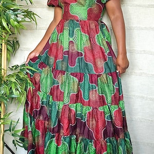 May include: A tiered maxi dress with an off-the-shoulder neckline and short puff sleeves. The dress is made of a colorful fabric with a geometric pattern in shades of green, red, and gold.