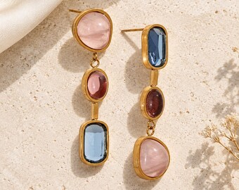 May include: A pair of gold-tone drop earrings featuring three vertically aligned stones each. The left earring has a pale pink, a deep pink, and a blue stone. The right earring has a blue, a deep pink, and a pale pink stone.