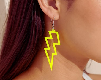 May include: Bright neon yellow lightning bolt earrings. These earrings are a fun and bold accessory, featuring a simple, outlined design. The earrings hang from a silver-colored hook.