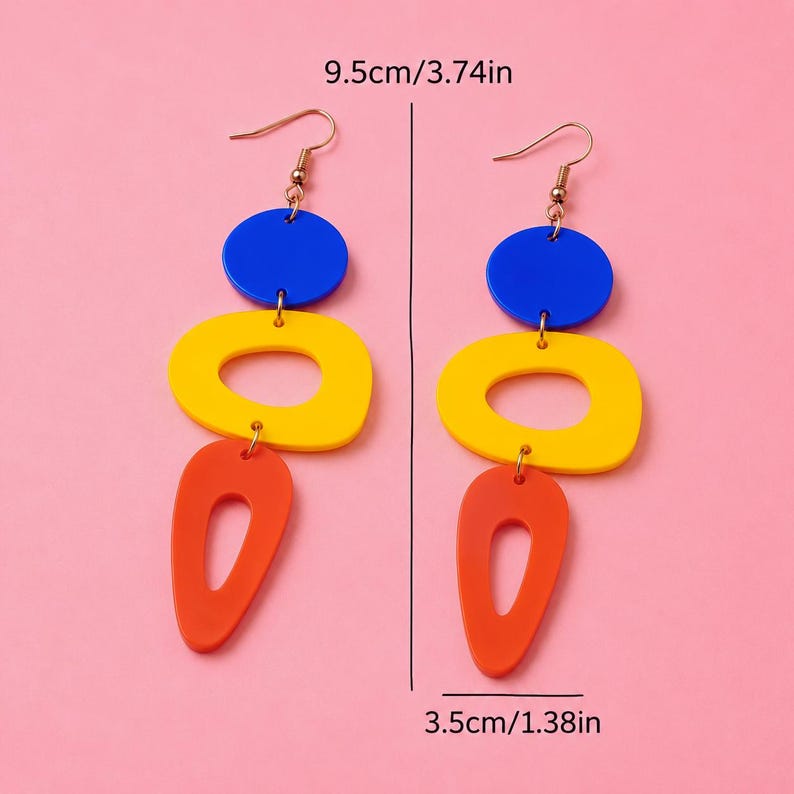May include: A pair of colorful dangle earrings. Each earring features a blue circle, a yellow oval, and an orange teardrop shape. The earrings are 3.74 inches long and 1.38 inches wide.