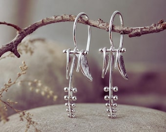 May include: A pair of silver drop earrings featuring a vertical bar design with small spherical beads arranged in a row. Each earring includes a curved hook wire and two small, textured leaf-shaped accents at the top of the central bar.