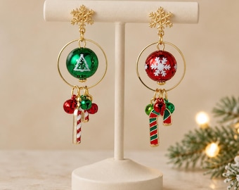 May include: A pair of gold-tone dangle earrings featuring a snowflake stud, a circular frame, and a central sphere. The left earring has a green sphere with a white tree, and the right has a red sphere with a white snowflake. Both include candy cane charms.