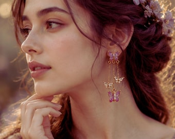 May include: Dangling butterfly earrings with purple and clear accents. The earrings feature three butterflies of varying sizes suspended from a gold chain. The top butterfly is larger and has purple wings, while the smaller butterflies have clear wings.