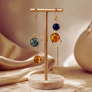May include: Gold-toned metal earring display stand with two pairs of dangling earrings. Each earring features a combination of colored glass beads and a gold-tone hoop. The beads are in shades of blue, green, and amber.