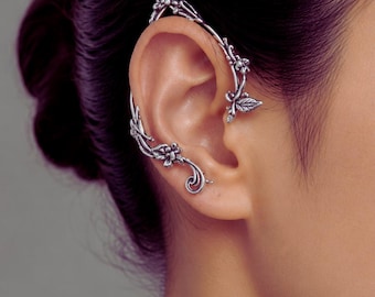 May include: Silver-toned ear cuff featuring a floral and leaf design. The cuff curves along the ear, with detailed flowers and leaves. The jewelry piece is worn on the ear, showcasing an elegant, nature-inspired aesthetic.