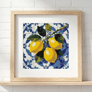 May include: A framed cross-stitch artwork featuring three bright yellow lemons on a branch with green leaves. The background is a blue and white tile pattern. The artwork is displayed in a light wood frame.