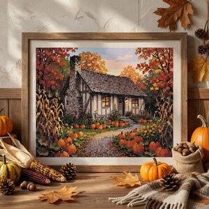 May include: A framed cross-stitch art piece depicting a cottage in an autumn landscape with orange pumpkins, yellow and red trees, and a stone chimney. The scene features a winding path leading to the house, surrounded by fall foliage and harvest decor.