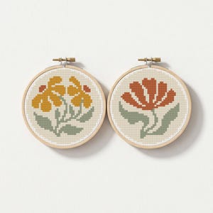 May include: Two floral cross-stitch embroidery hoops. One features yellow flowers and the other a red-orange flower, both with green leaves. The designs are set against a cream-colored background within wooden hoops, perfect for wall decor.
