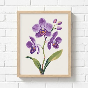 Puede incluir: Un patrón de punto de cruz de una orquídea morada con hojas verdes y capullos cerrados, representado en un estilo pixelado sobre un fondo de cuadrícula blanca, dentro de un marco de madera clara con un perfil rectangular sencillo.