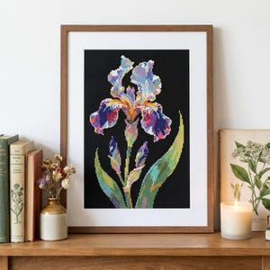 May include: A framed cross-stitch embroidery featuring a vibrant iris flower with purple, blue, and yellow petals against a solid black background, accompanied by green leaves and two unopened buds, displayed in a simple wooden frame.